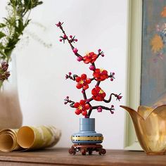 a vase filled with red flowers sitting on top of a wooden table next to other vases