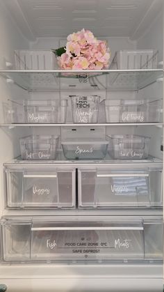 an open refrigerator filled with lots of plastic containers and flowers on the shelf above it