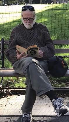 an old man sitting on a bench reading a book