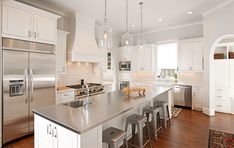 a large kitchen with stainless steel appliances and white cabinets, along with hardwood flooring