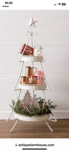 three tiered christmas tree with gifts on top and presents in the bottom, sitting against a white wall