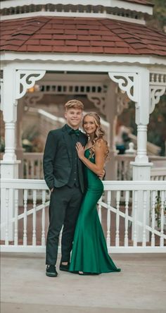 a man and woman standing in front of a gazebo wearing formal wear, posing for the camera