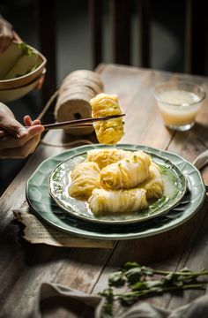 a person is holding chopsticks over some food on a green and white plate