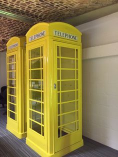 two yellow telephone booths sitting next to each other on a wooden floor in an office building