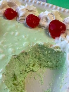 a green cake with white frosting and cherries on the top is ready to be eaten