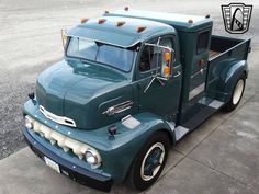 an old green truck is parked on the street