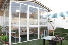 an enclosed patio with green furniture and potted plants on the grass in front of it