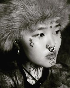 a woman with piercings on her face and nose is looking at the camera while wearing a fur hat