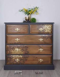 a wooden dresser with gold designs on the drawers and flowers in a vase next to it