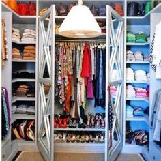 an open closet with clothes and shoes on the bottom shelf, next to a lamp