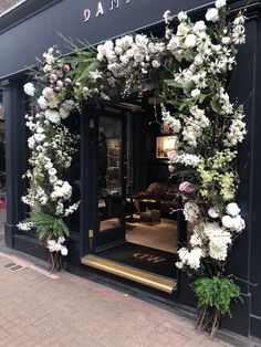 a store front decorated with white flowers and greenery on the outside, along with black doors