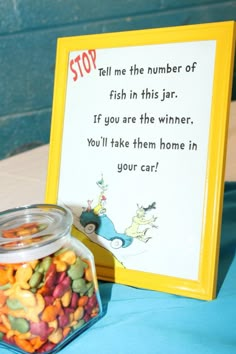 a glass jar filled with candy sitting next to a sign that says, stop tell me the number of fish in this jar