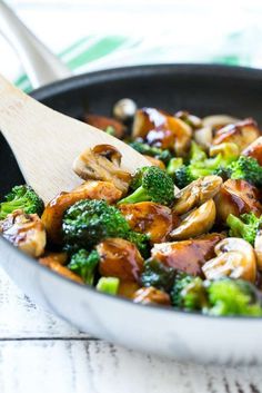 broccoli and mushrooms are being cooked in a skillet with a wooden spoon