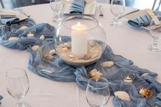 a table topped with a bowl filled with sand and a candle next to wine glasses