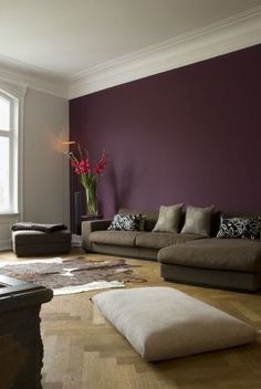 a living room filled with furniture and a purple wall behind the couch is a large window