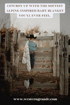 a little boy leaning on a fence with a cowboy hat and blanket over his shoulder