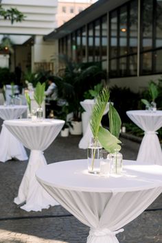 tables with white tablecloths and green plants in vases on the side walk