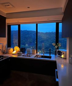 a kitchen with a large window overlooking the trees outside at night, and lit candles on the counter