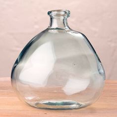 a clear glass vase sitting on top of a wooden table next to a pink wall