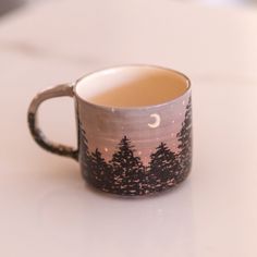 a coffee cup sitting on top of a table with trees painted on it's side