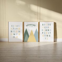 three posters with numbers and mountains are on the floor in front of a beige wall