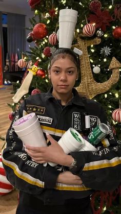 a woman holding two cups in front of a christmas tree with decorations on it and a hat on her head