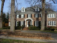 a large brick house with black shutters and white trim on the front door is surrounded by leafy trees