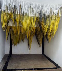 an art installation consisting of yellow and white sticks hanging from the ceiling in a room with concrete flooring