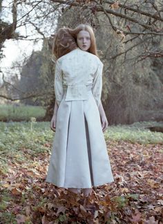 a woman is standing in the leaves with her back to the camera, wearing a white dress