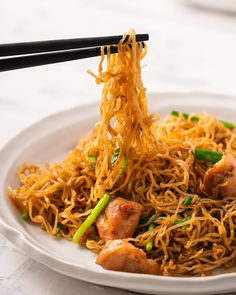 a white plate topped with noodles and meat next to chopsticks on a table