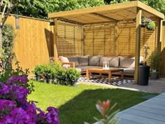 an outdoor living area with purple flowers in the foreground and a wooden gazebo