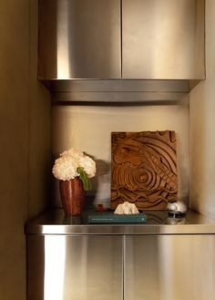 a vase with flowers on top of a stainless steel cabinet in a room that looks like it has been built into the wall