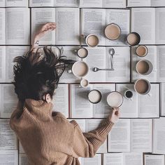 a woman laying on top of an open book next to coffee cups and spoons