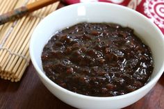 a white bowl filled with black beans on top of a wooden table next to chopsticks