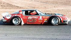 a red race car driving on a track in the desert with no cars behind it