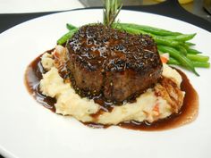 a white plate topped with meat and mashed potatoes covered in gravy next to green beans