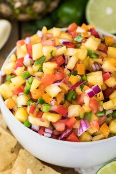 a white bowl filled with pineapple salsa surrounded by tortilla chips and lime wedges