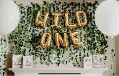 some balloons that say wild one are in front of a wall with ivy and white balloons