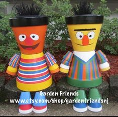 two colorful pots with faces and hair on them sitting next to each other in front of some bushes