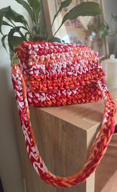 an orange and white purse sitting on top of a wooden table next to a potted plant