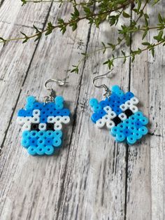 two blue and white beads are hanging from earrings on a wooden table next to a plant