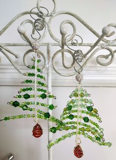 two christmas trees are hanging from a metal rack with green and red beaded ornaments