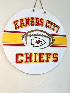 kansas city chiefs football sign hanging on the side of a white wall with red and yellow stripes