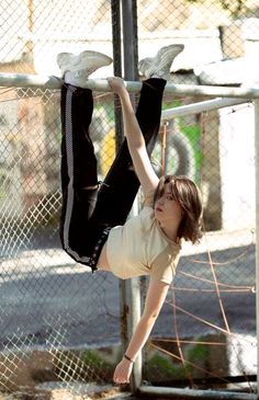 a young boy is hanging upside down on a pole in front of a chain link fence