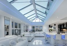 a living room filled with white furniture and a skylight over the dining table area