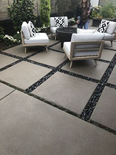 a woman standing next to two couches and chairs on a patio with gravel in the middle