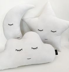 three pillows with eyes and eyelashes on them sitting next to each other in front of a clock