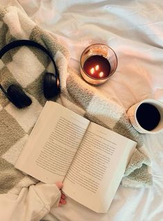 an open book and headphones on a bed with a cup of coffee next to it