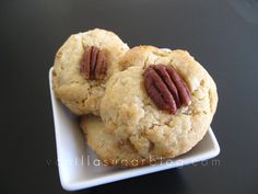 three cookies with pecans in the middle on a white plate sitting on a black table