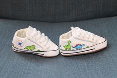 two white shoes with dinosaurs painted on them are sitting on a blue couch next to each other